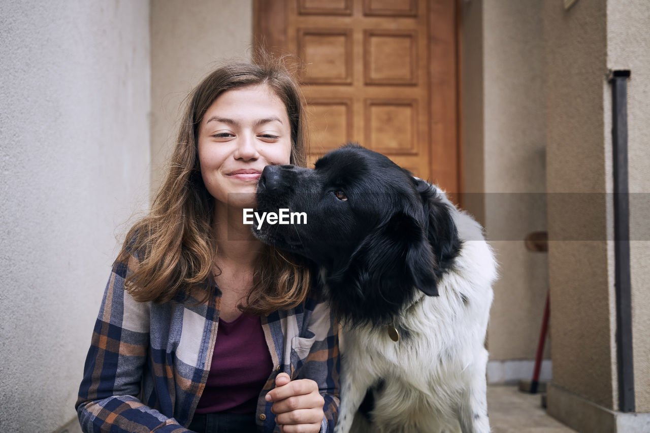 Portrait of happy teenager girl sitting with her czech mountain dog against against door of house.