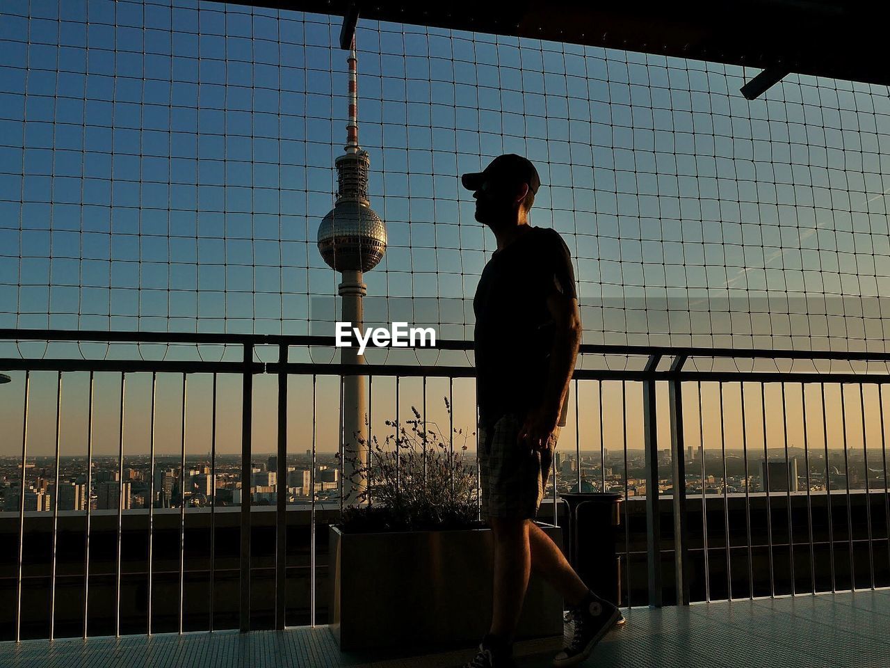 Silhouette man walking by railing against fernsehturm during sunset