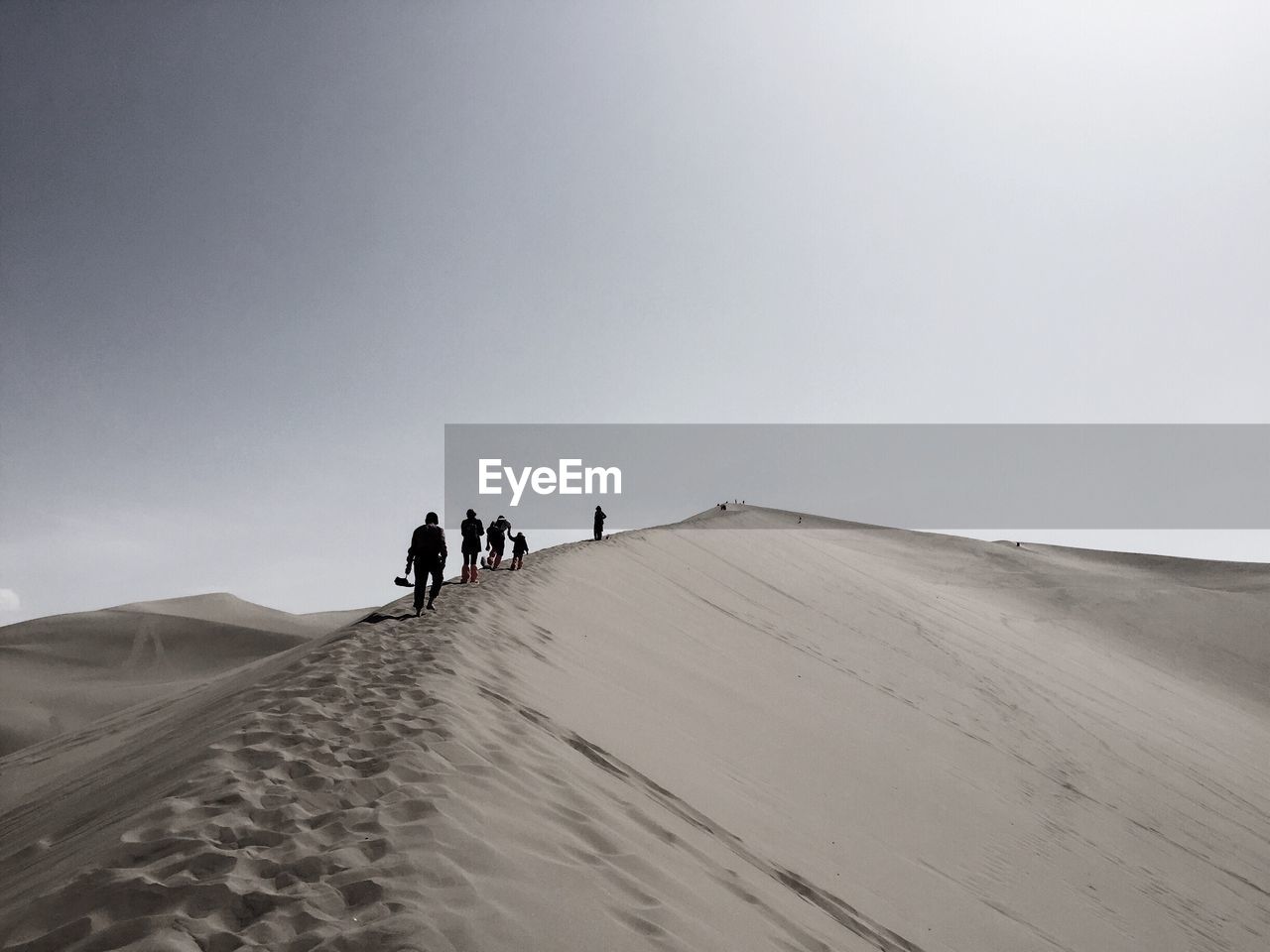 Rear view of people walking on sand dune at desert against clear sky