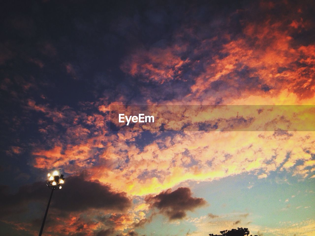 Low angle view of illuminated floodlight against cloudy sky during sunset