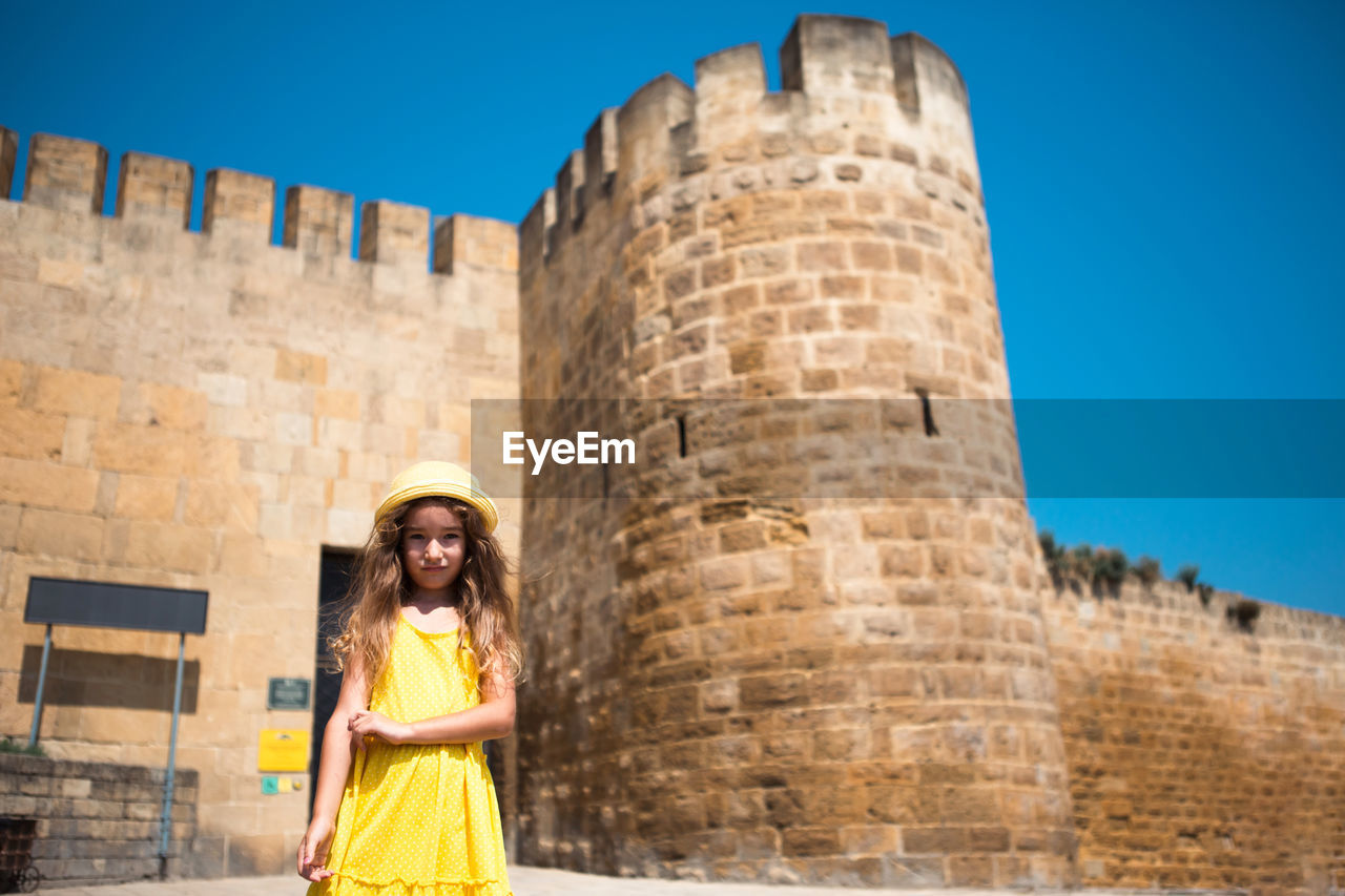 portrait of woman standing against building against clear blue sky