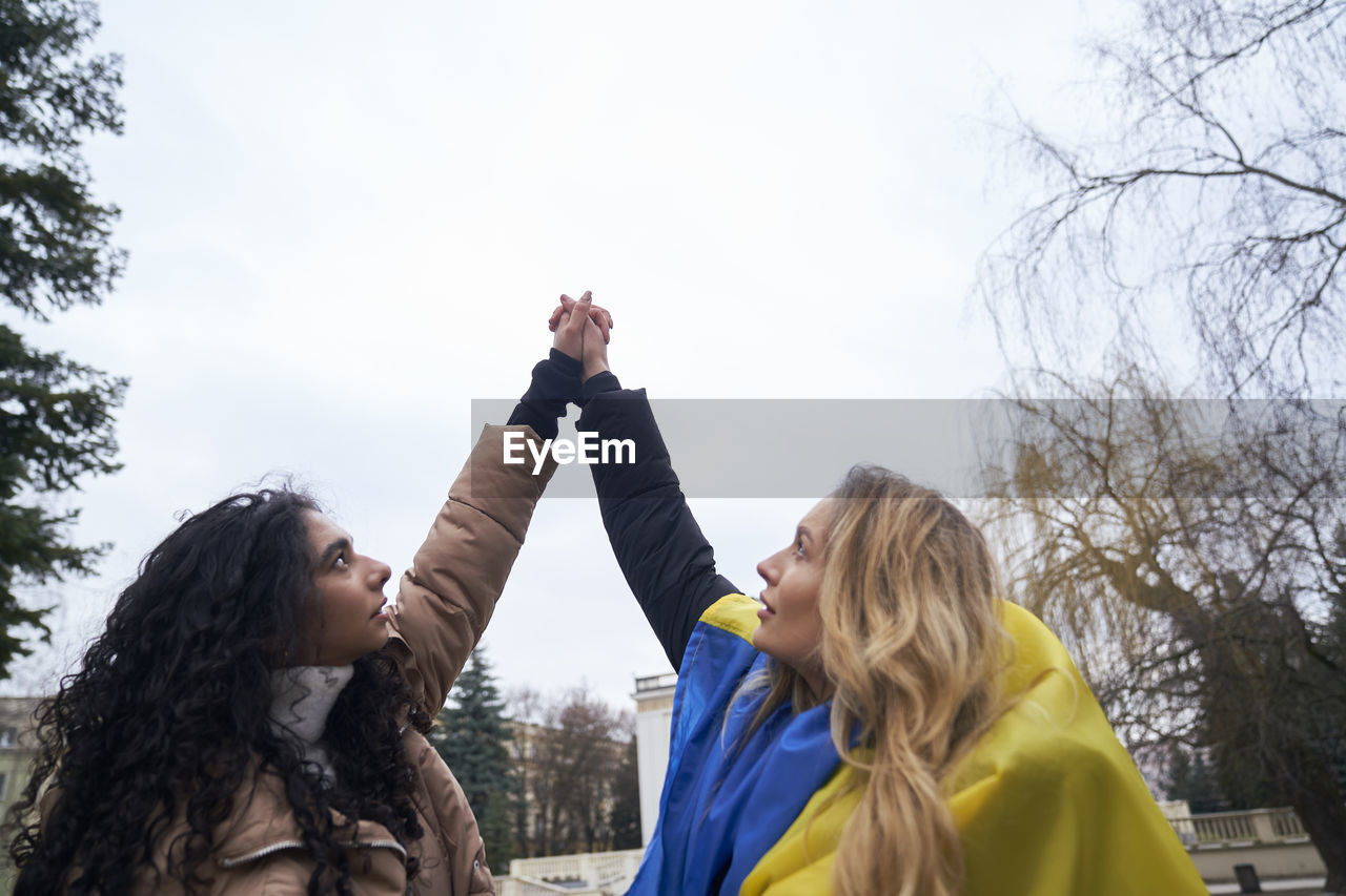 Female friends holding hands against sky