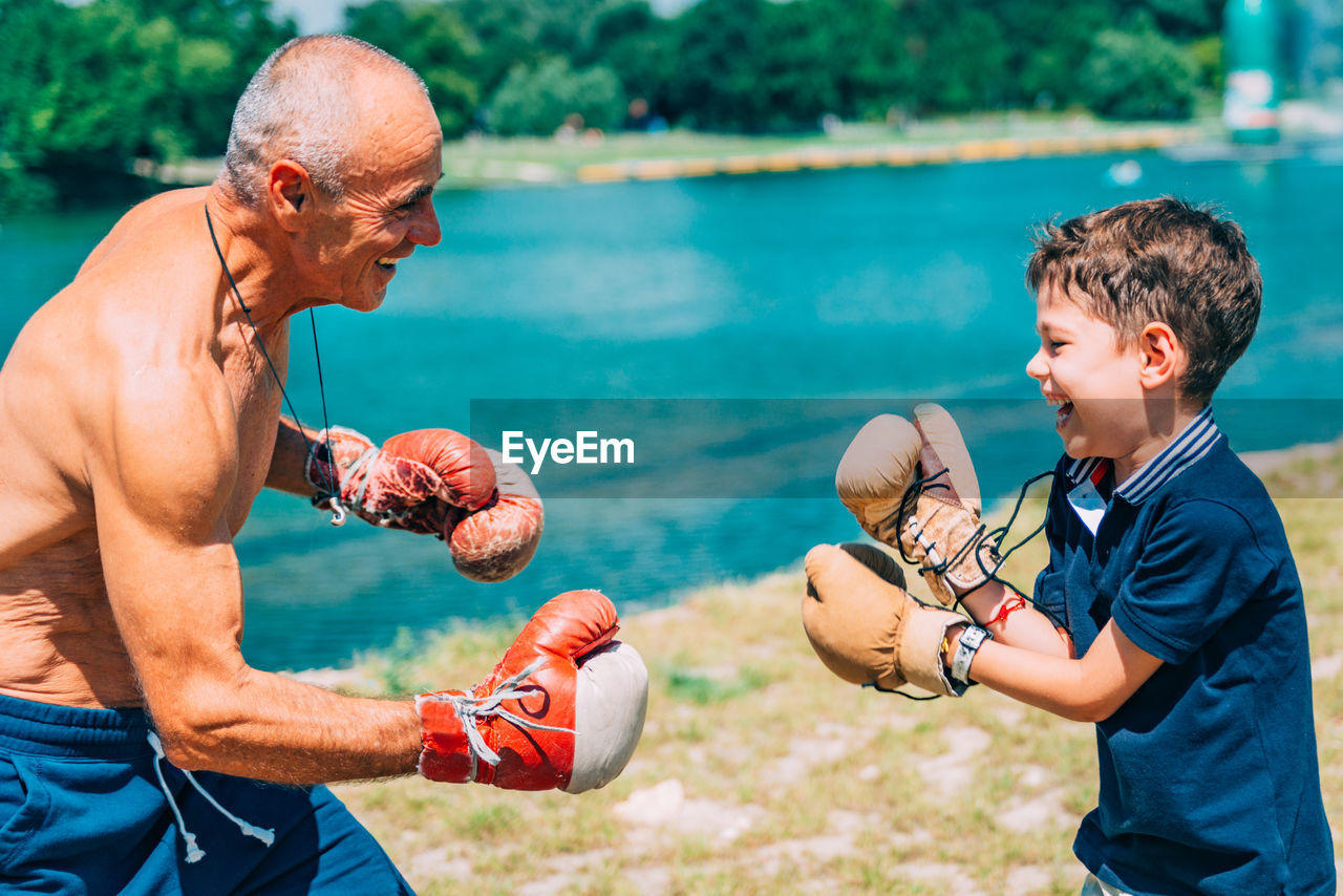 Shirtless grandfather with grandson boxing by swimming pool