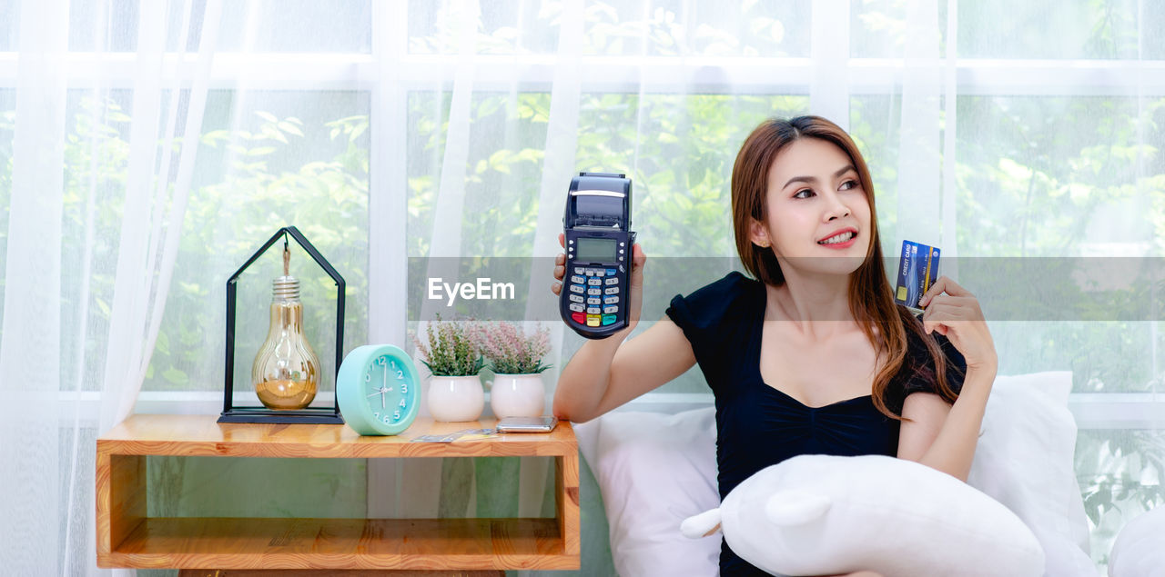 YOUNG WOMAN SMILING WHILE SITTING ON SOFA AT HOME