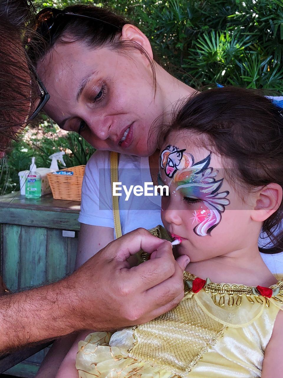 Mother looking at artist applying paint on lips of daughter