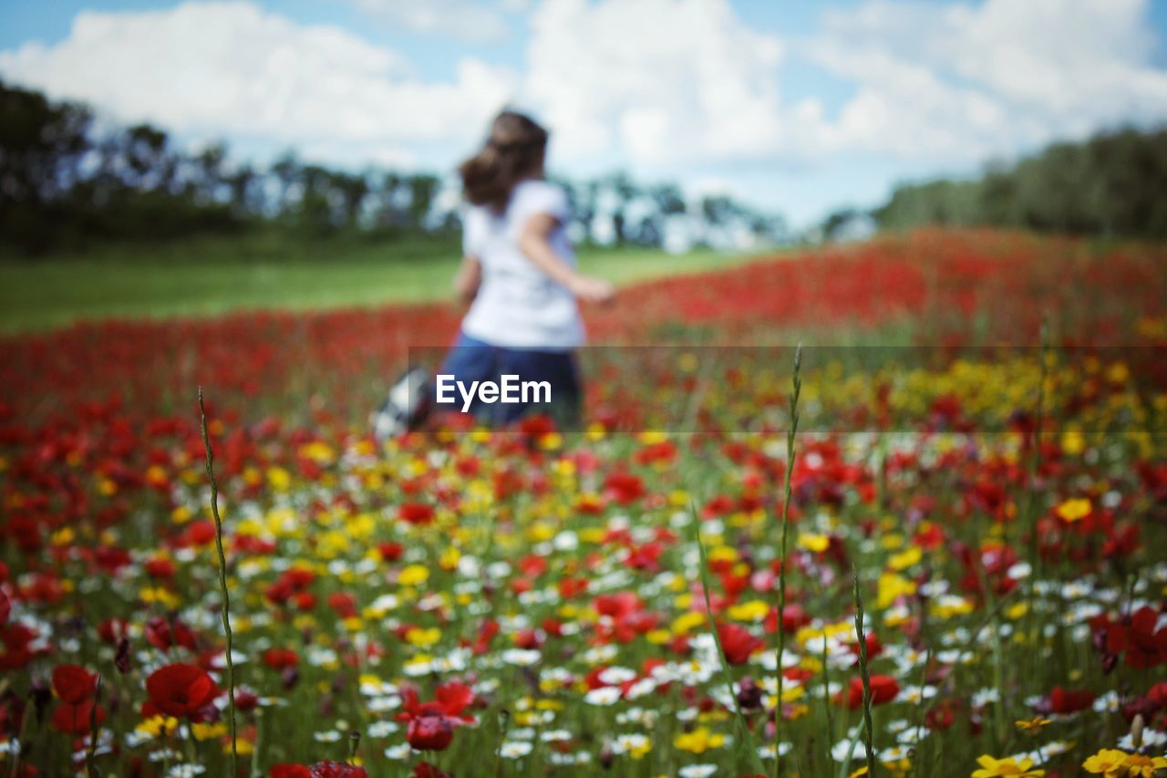 WOMAN STANDING ON FIELD OF FLOWERING PLANTS