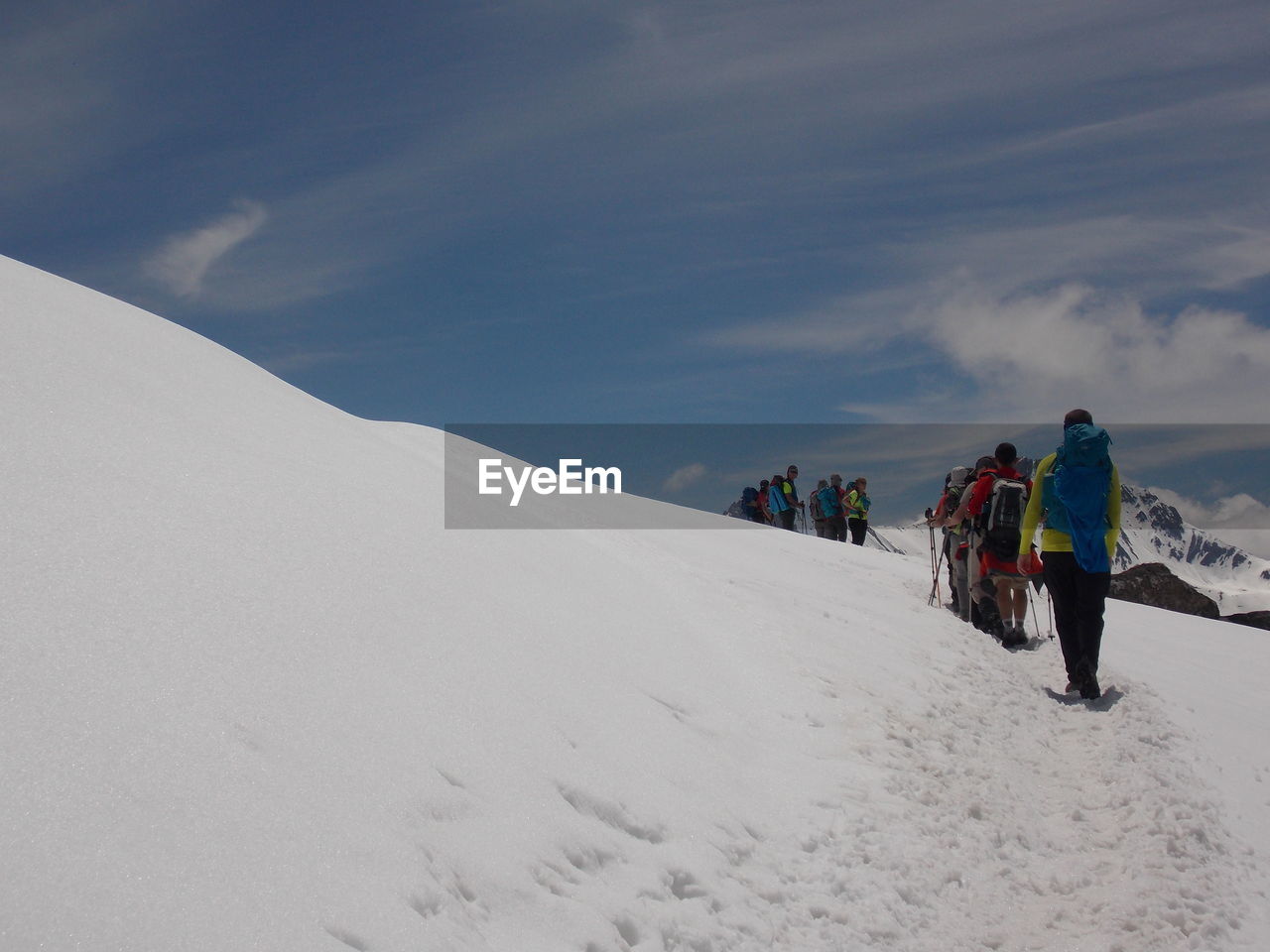 REAR VIEW OF PEOPLE WALKING ON SNOWCAPPED MOUNTAIN ROAD