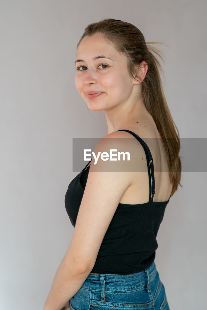 PORTRAIT OF SMILING WOMAN STANDING AGAINST WALL