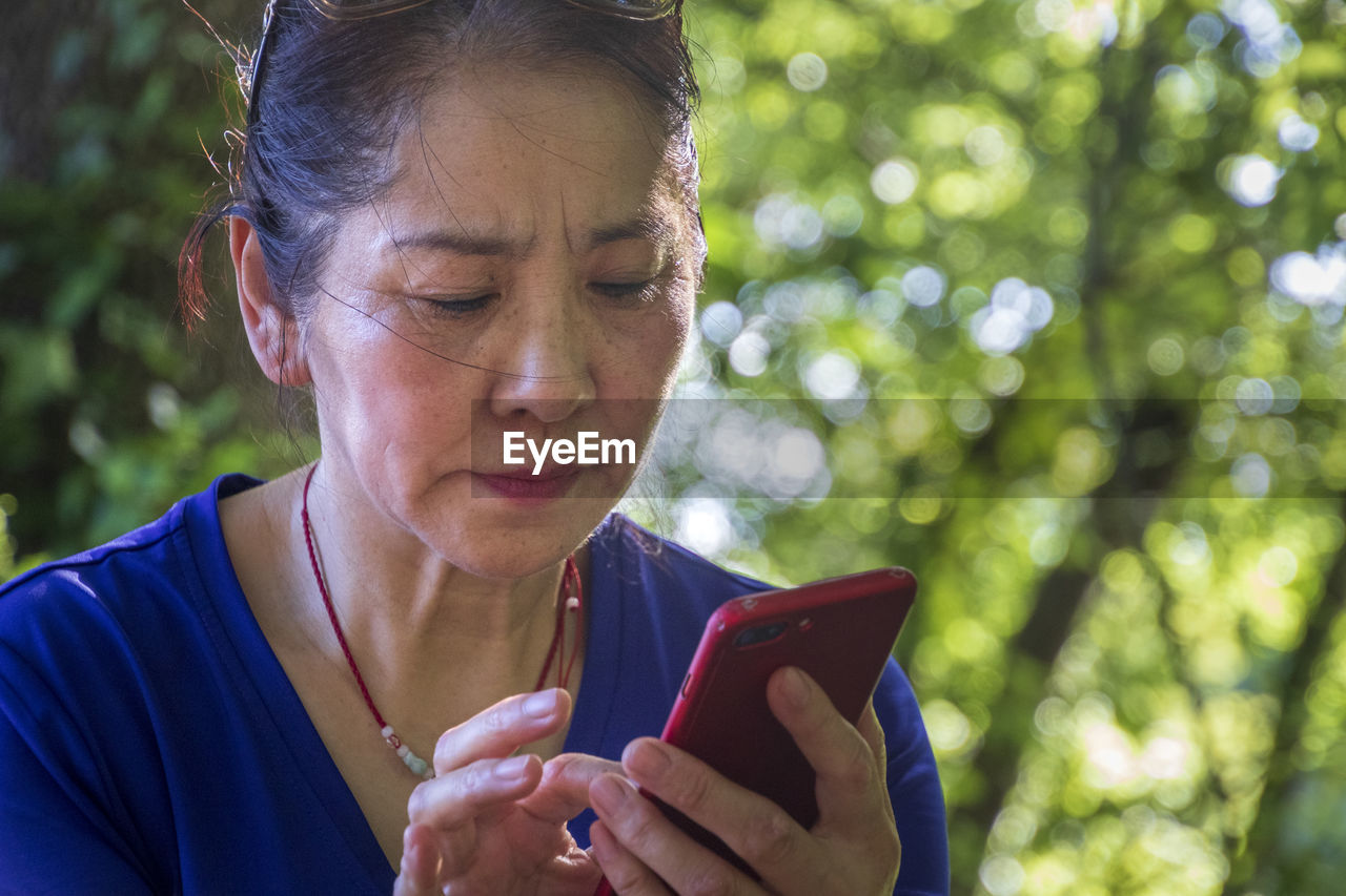 PORTRAIT OF WOMAN HOLDING SMART PHONE OUTDOORS