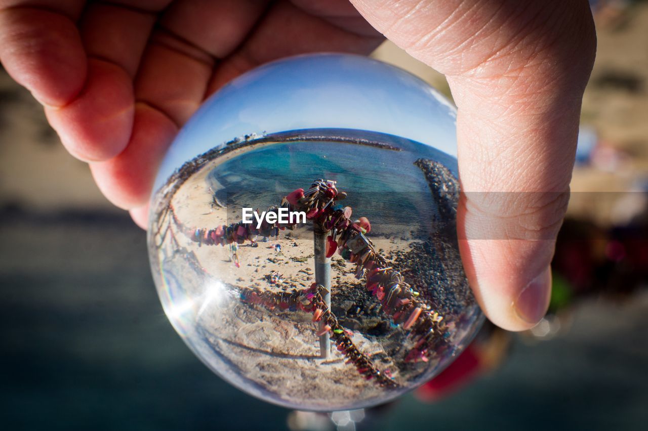 Close-up of hand holding crystal ball against sea