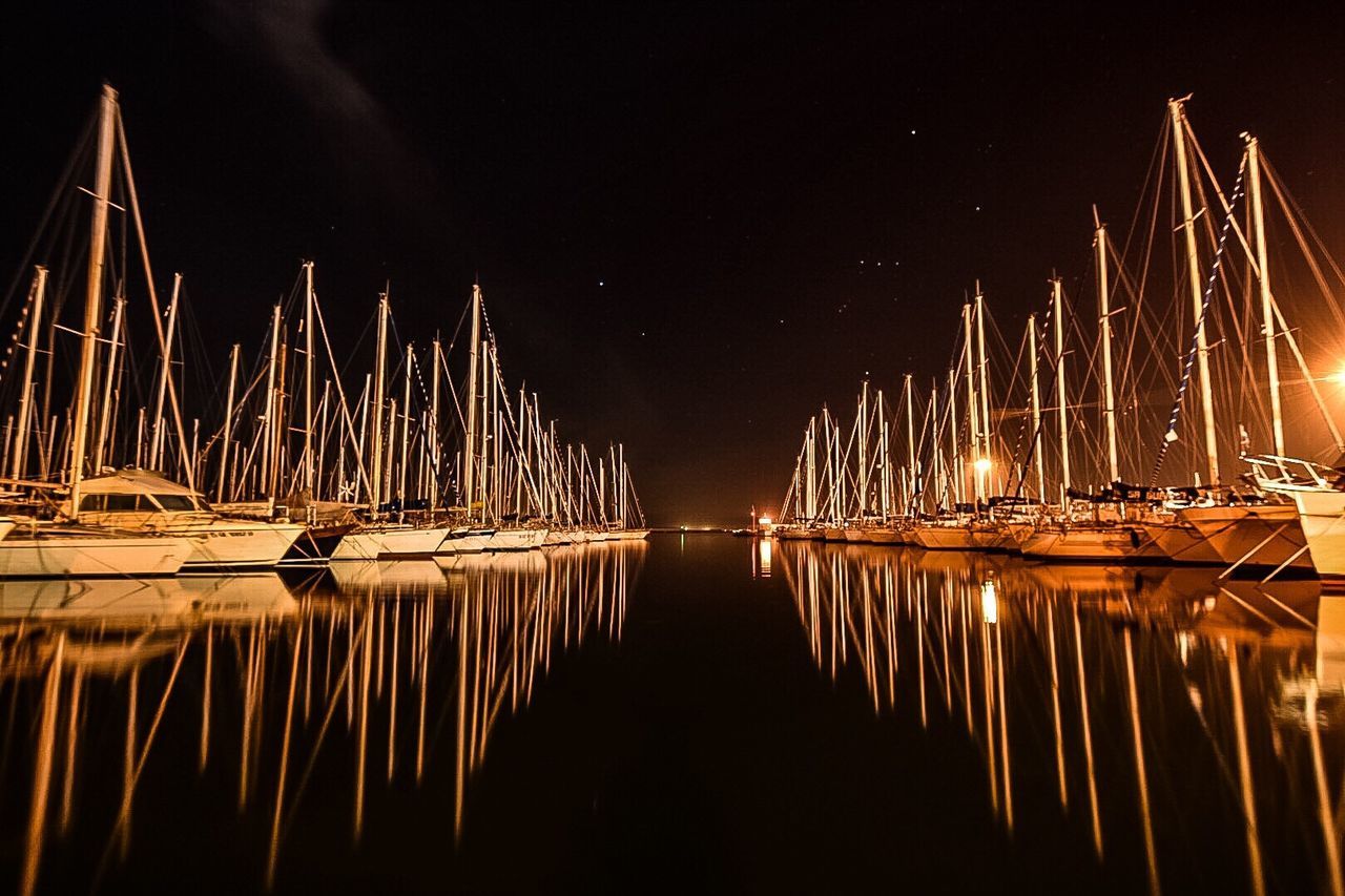 Reflection of boat mast on calm lake at night