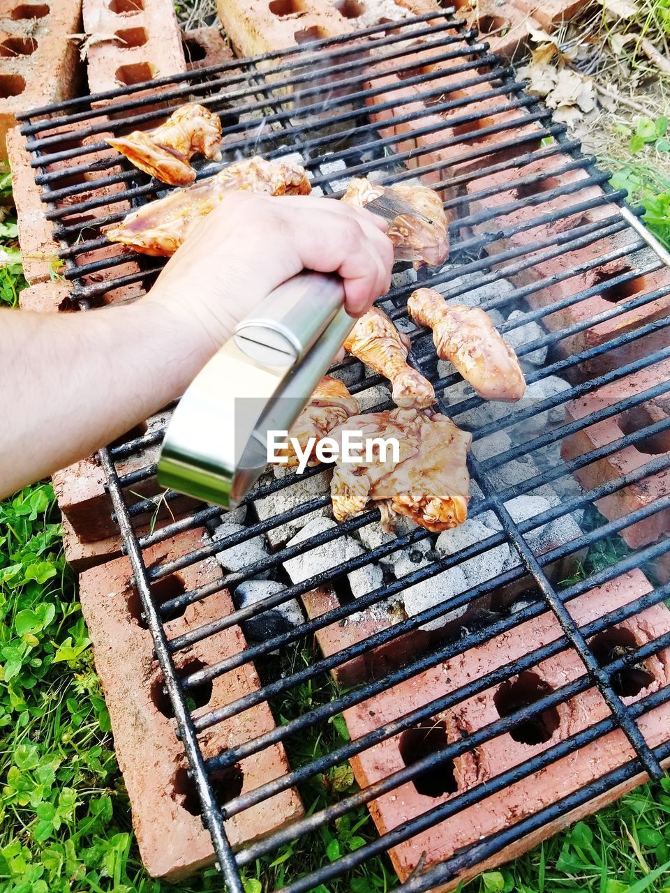 Cropped hand preparing meat on barbecue grill in yard