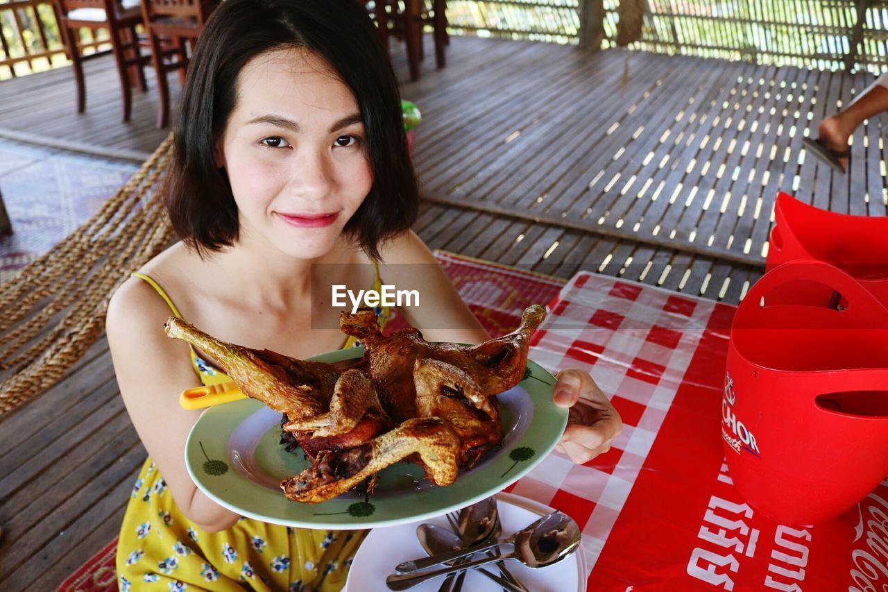 Portrait of young woman showing food while sitting at table in restaurant