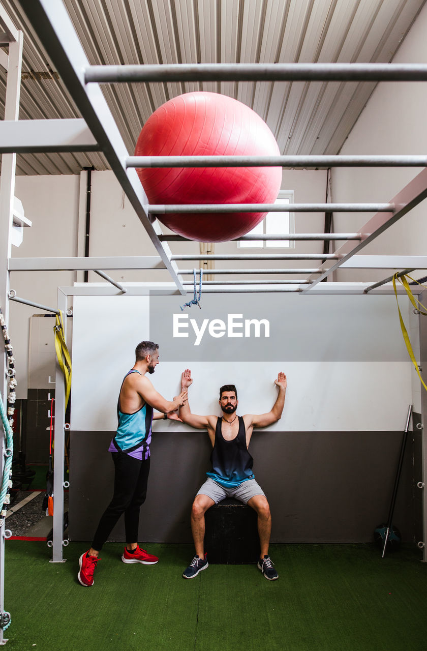 Young athletic male in sportswear performing squats while training in modern gym with instructor