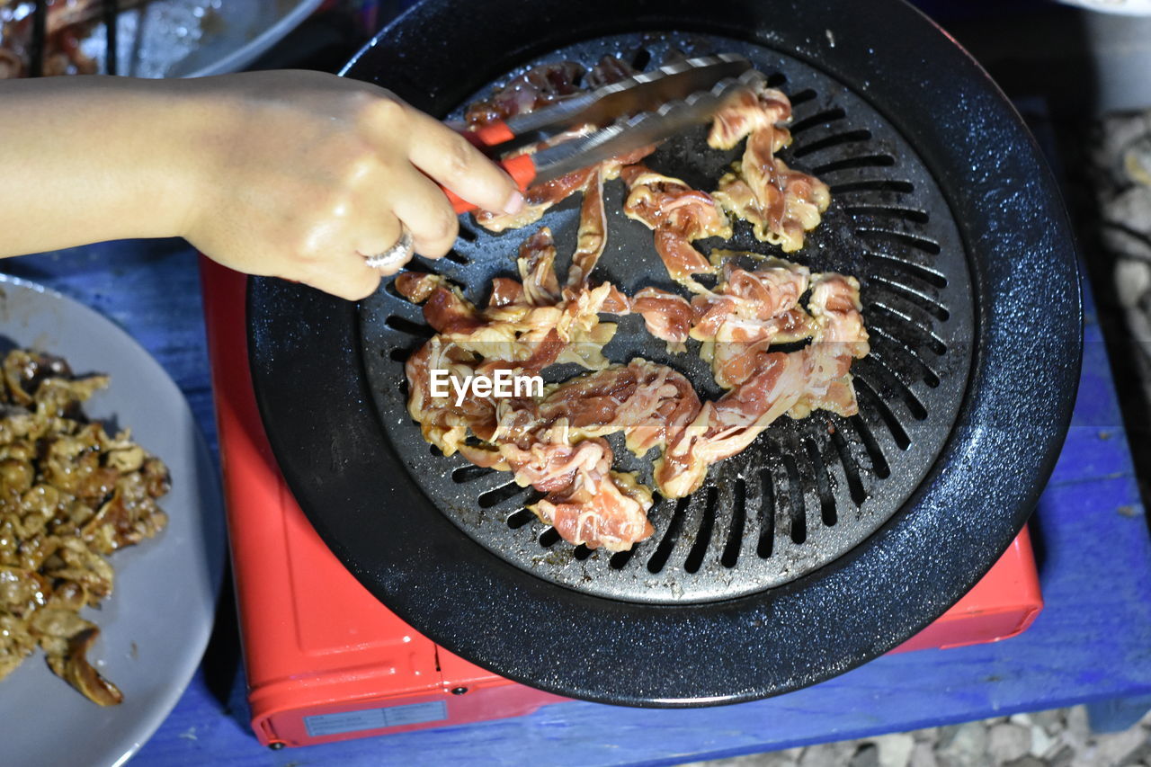 HIGH ANGLE VIEW OF PERSON PREPARING FOOD ON BARBECUE