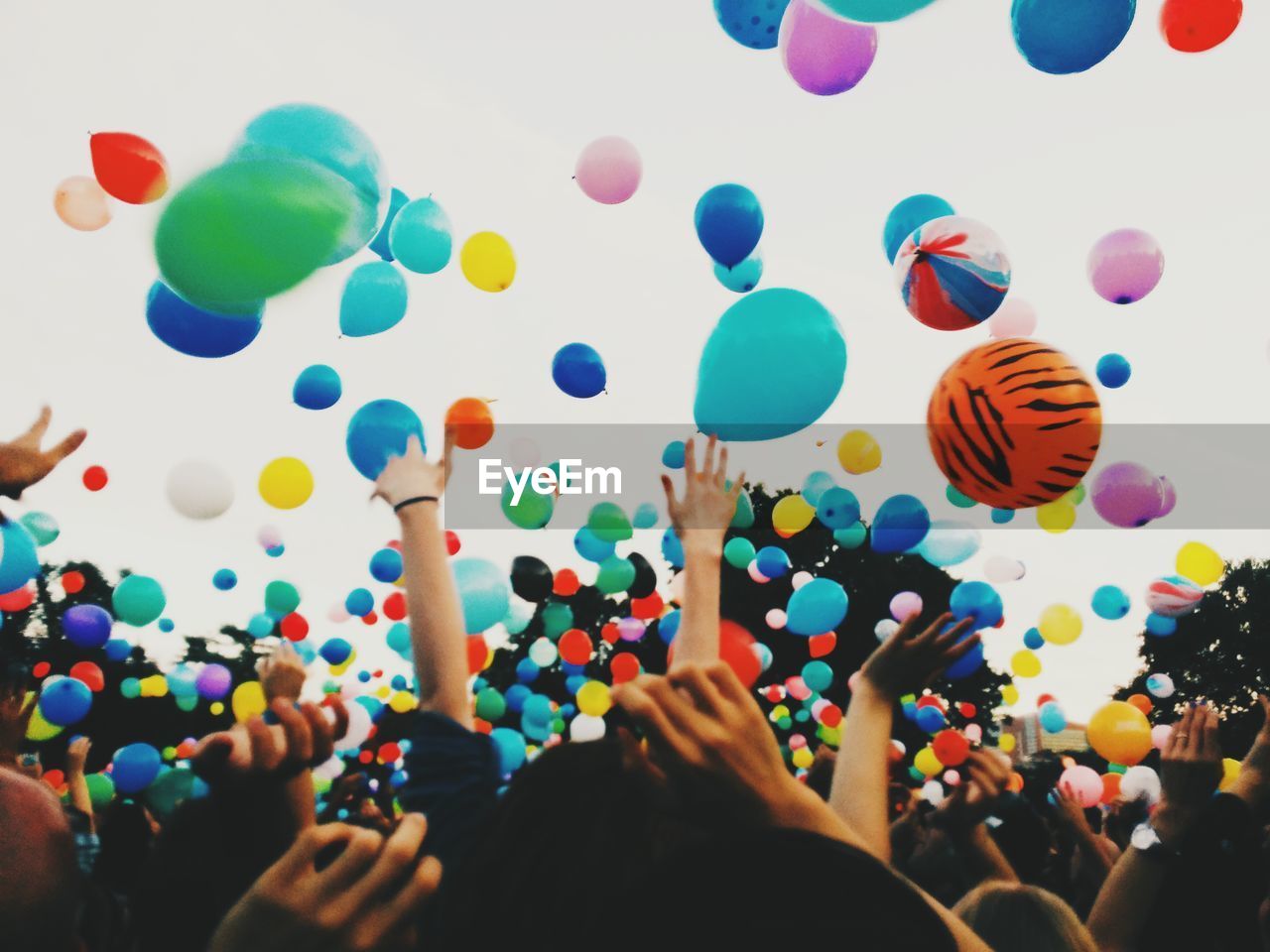 Crowd throwing colorful balloons against sky during festival