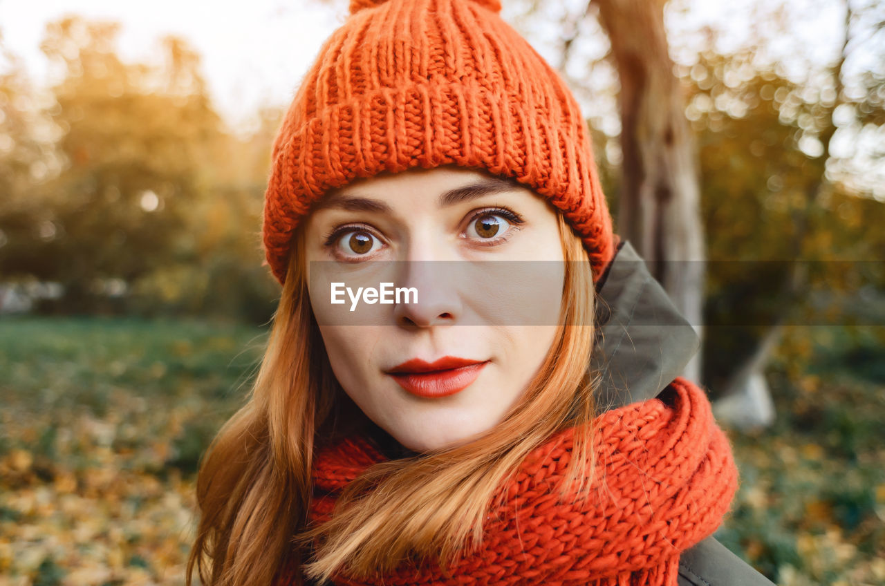 Bright cute young woman in orange warm knitted hat and scarf. autumn portrait close-up.