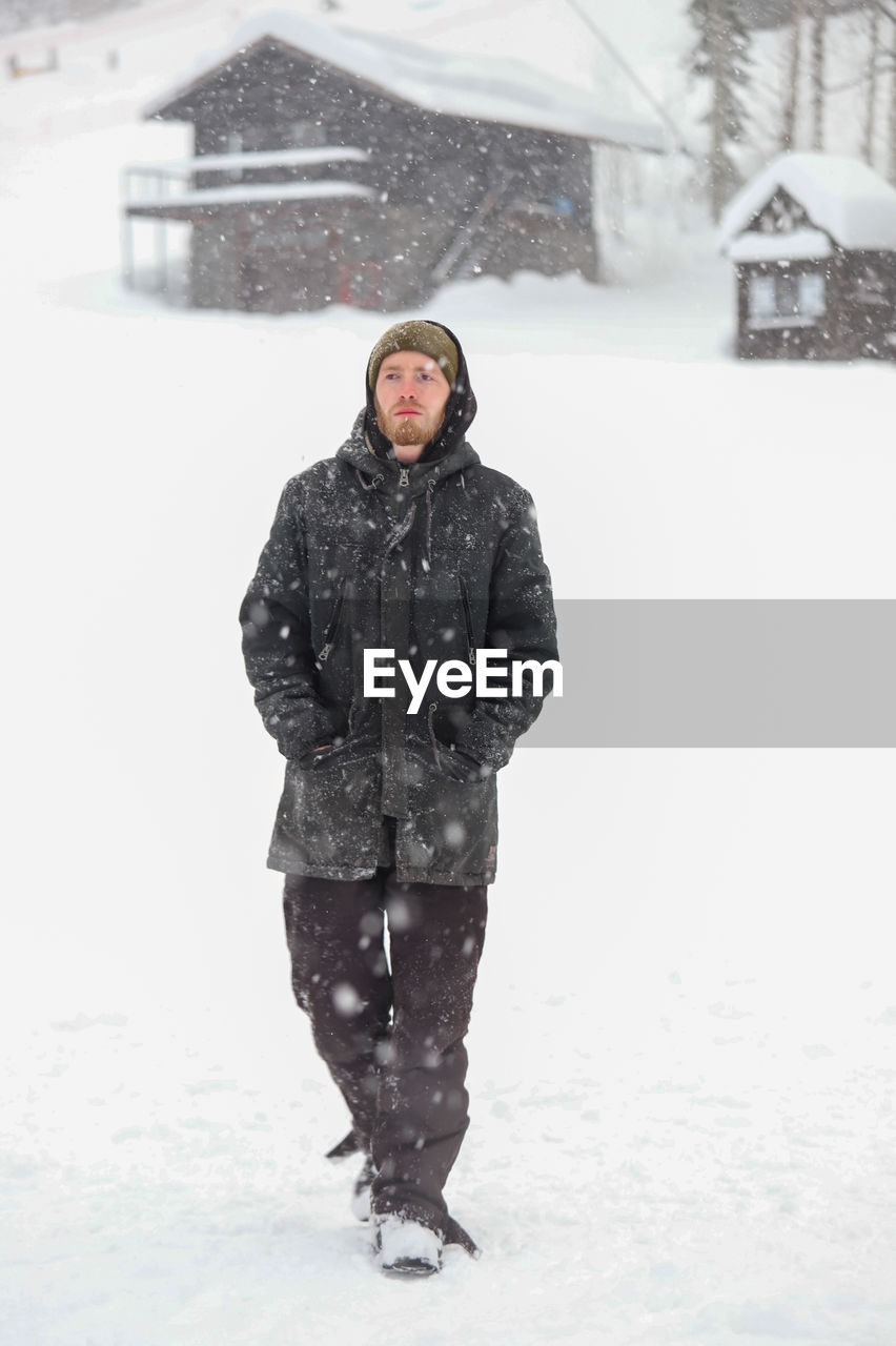 winter, cold temperature, snow, clothing, warm clothing, one person, adult, winter storm, snowing, blizzard, nature, footwear, full length, young adult, architecture, frozen, men, portrait, front view, freezing, coat, storm, hat, extreme weather, lifestyles, standing, smiling, leisure activity, day, environment, emotion, winter coat, outdoors, happiness, building exterior, snowflake, glove, white, looking at camera, ice