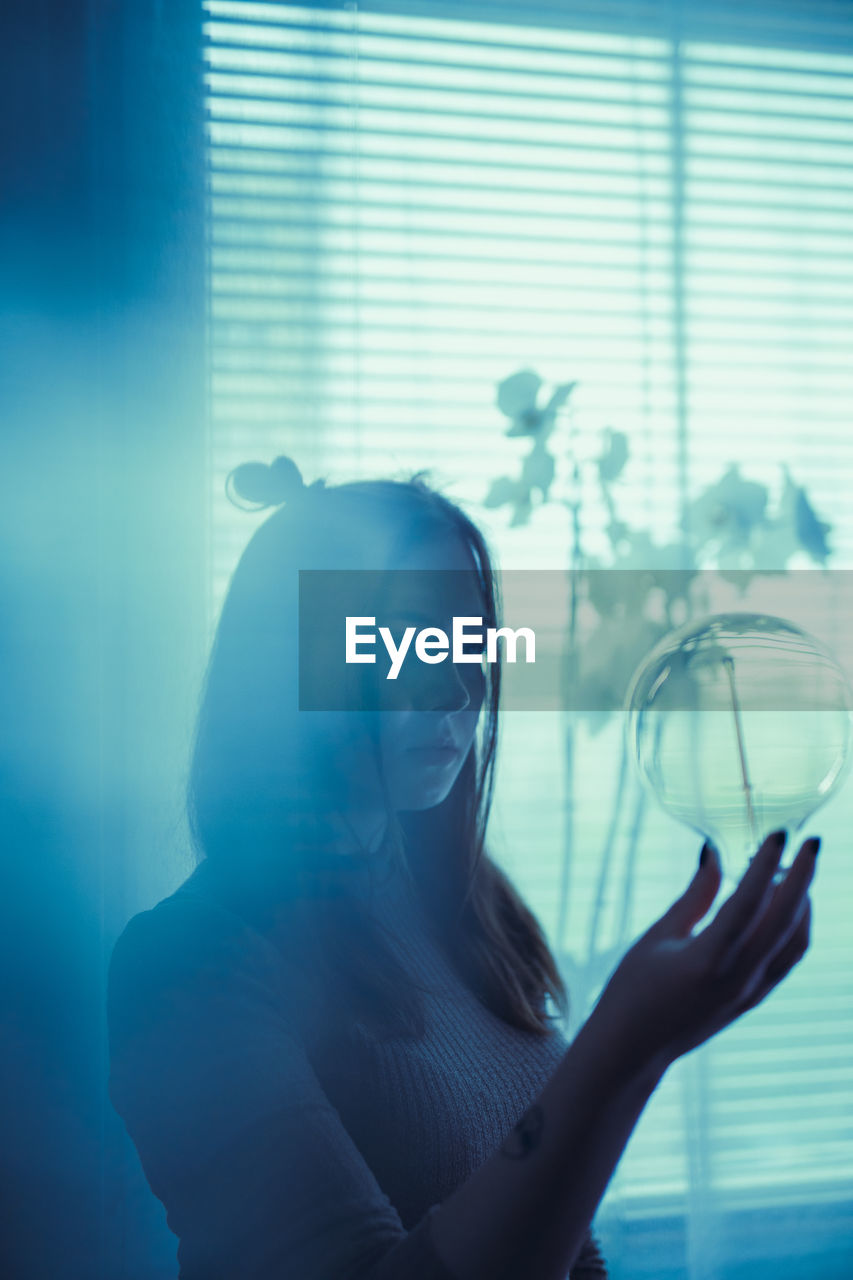 Portrait of young woman looking through window