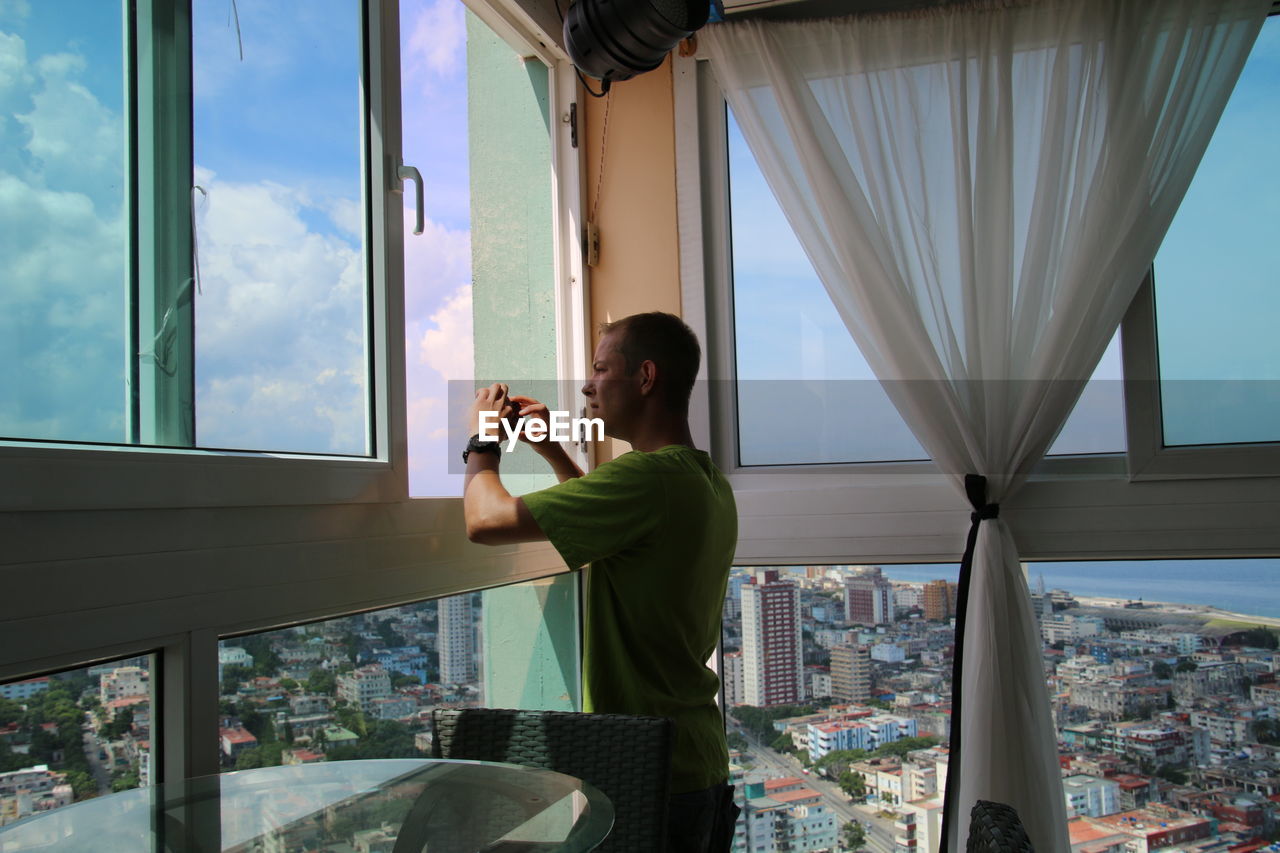 Man holding mobile phone while standing by window at home