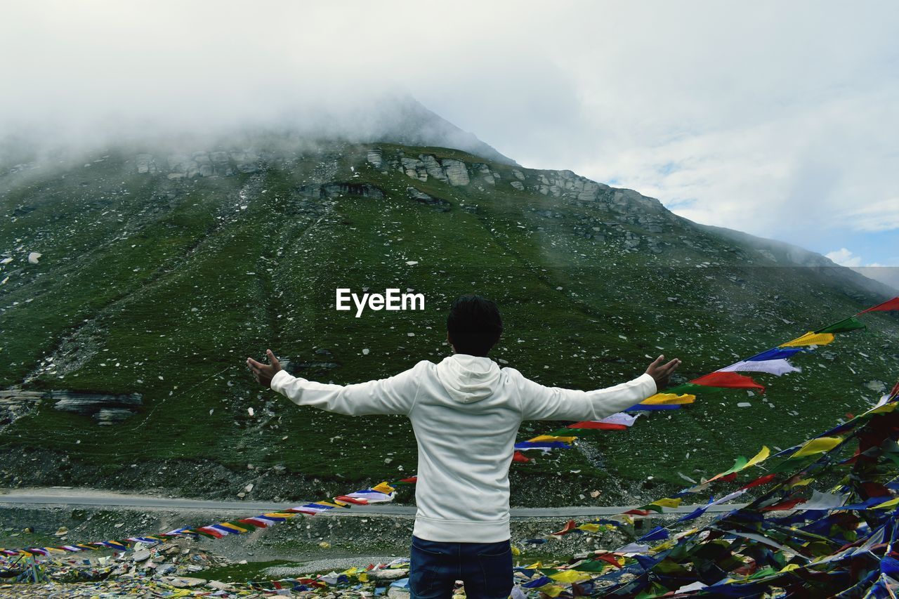 Rear view of man standing by prayer flags and mountain against sky