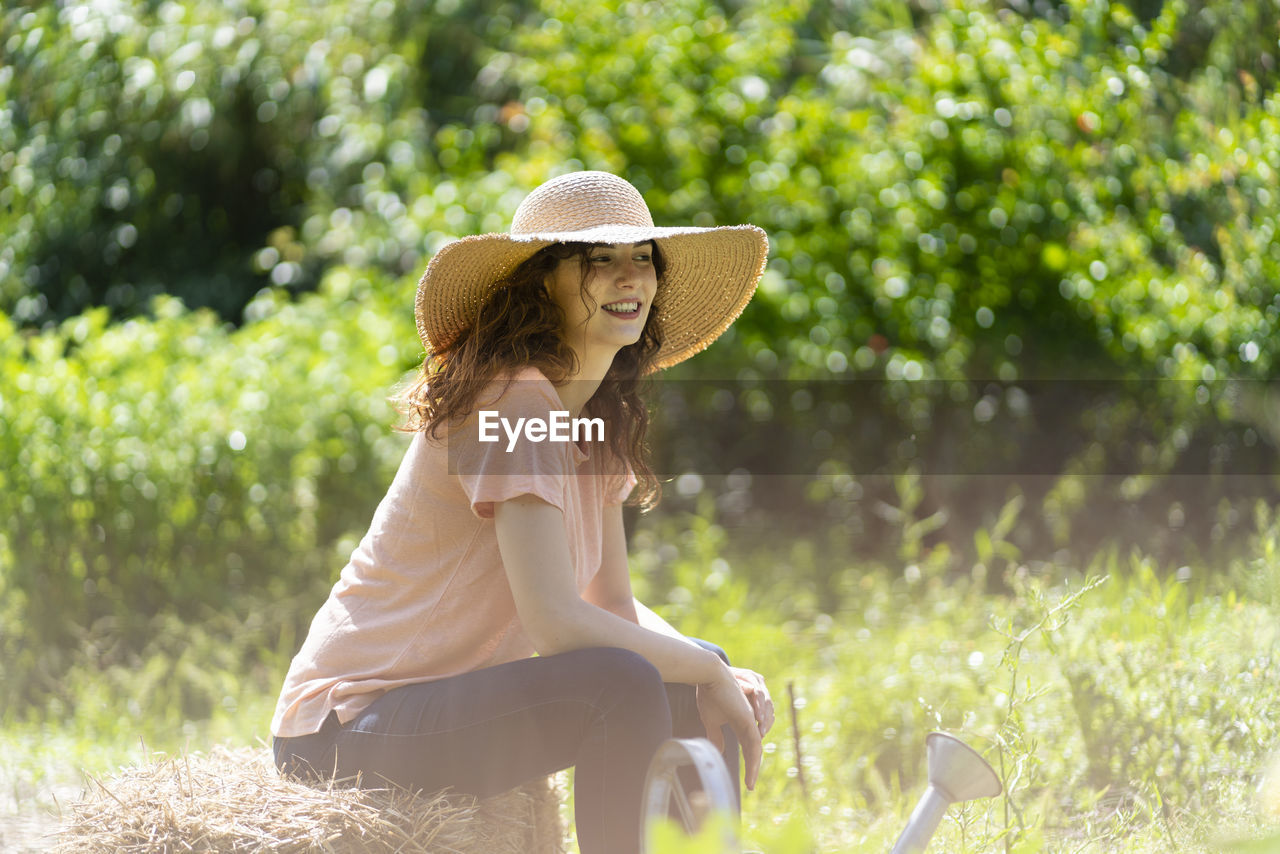 Woman with sun hat sitting on hay in garden during sunny day