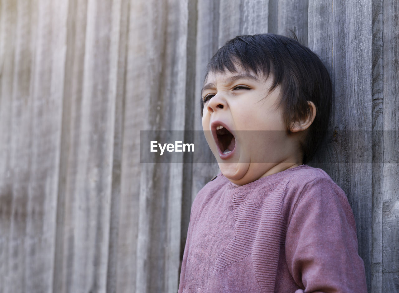 Boy yawning while looking away against wall