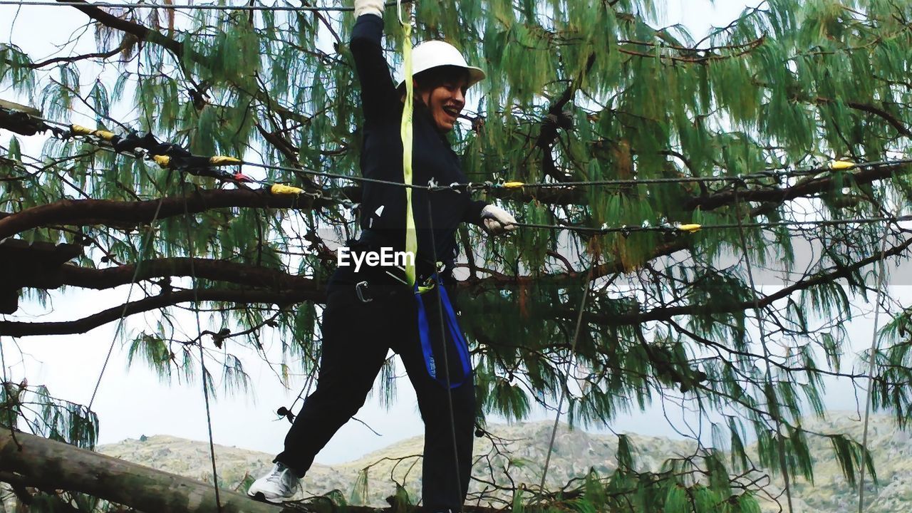 tree, plant, branch, one person, nature, jungle, adult, forest, protection, helmet, headwear, land, full length, flower, security, leisure activity, outdoors, safety harness, men, sports, growth, day, standing, green, low angle view, lifestyles, young adult, clothing, natural environment, person, sky, sports helmet