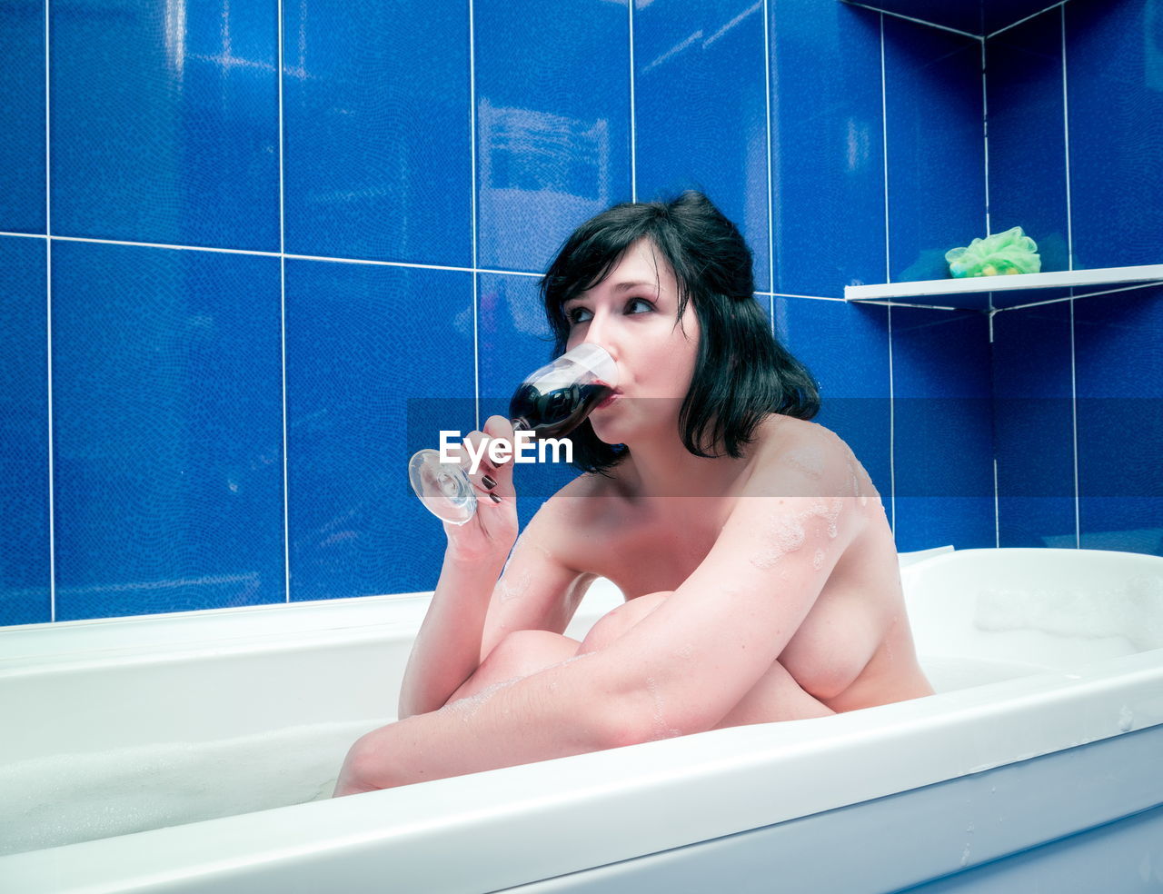 Naked woman drinking wine while sitting in bathtub