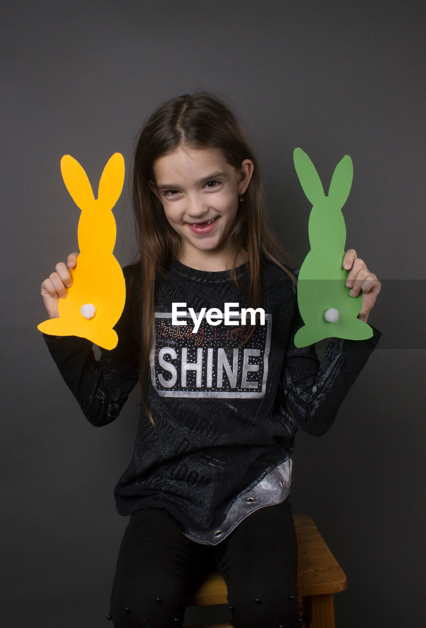 Portrait of smiling girl holding paper eater bunny against gray background