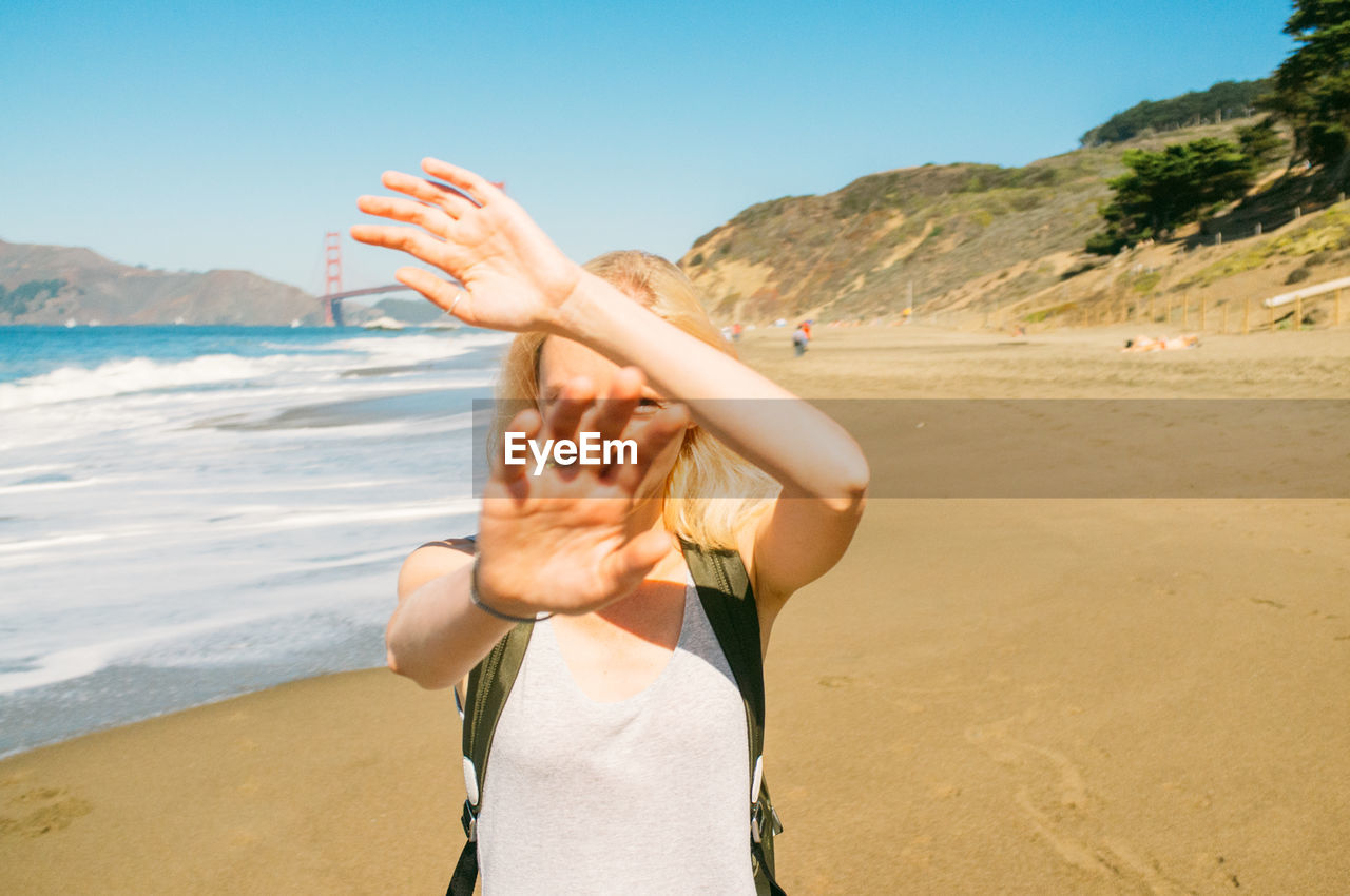 Portrait of woman covering face with hands at beach against clear sky