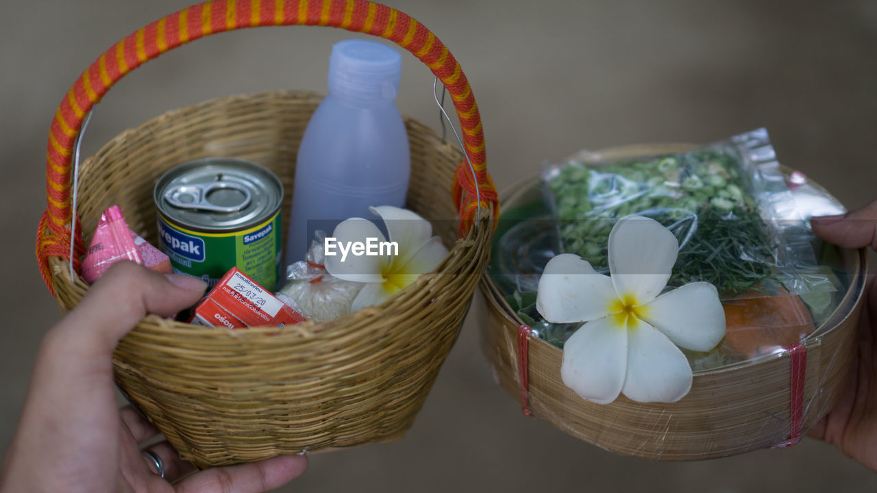 CLOSE-UP OF HAND HOLDING WHITE FLOWERS IN BASKET OF RED ROSES