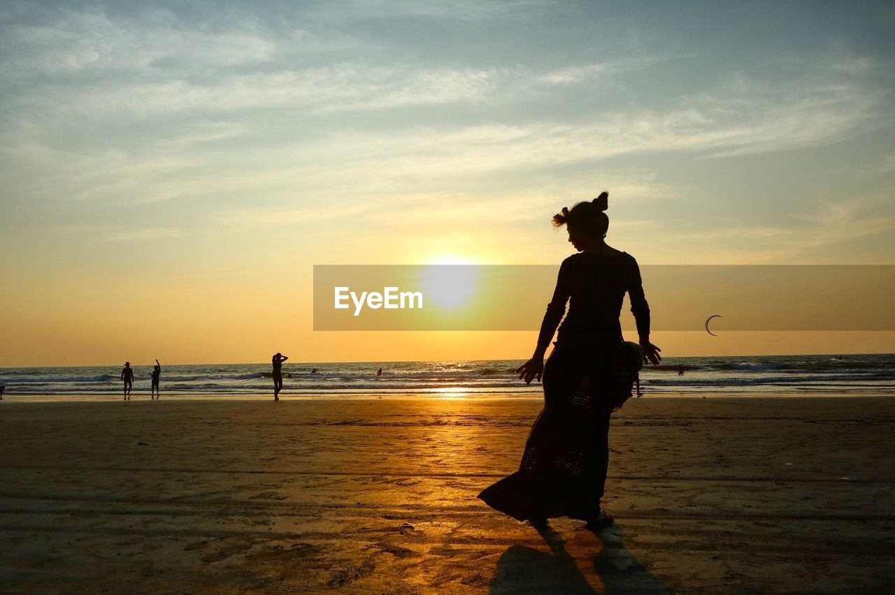 Silhouette woman standing at arambol beach against sky during sunset