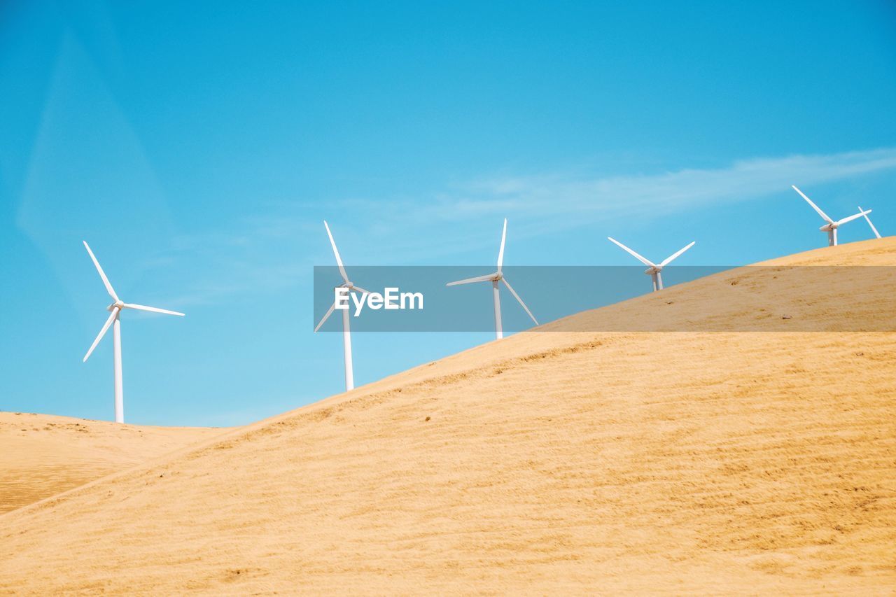 Wind turbines on desert against blue sky