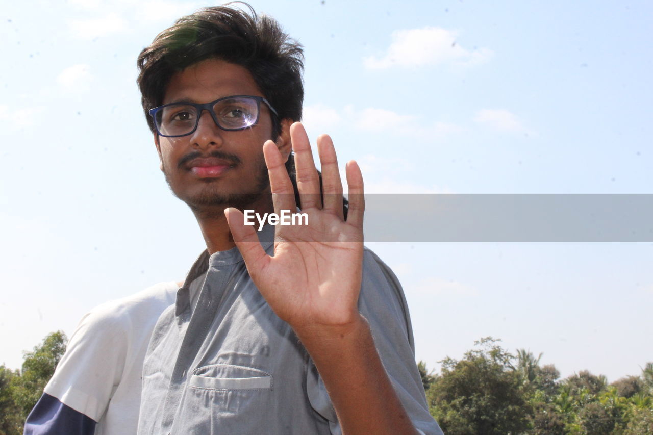 Portrait of young man showing stop gesture against clear sky