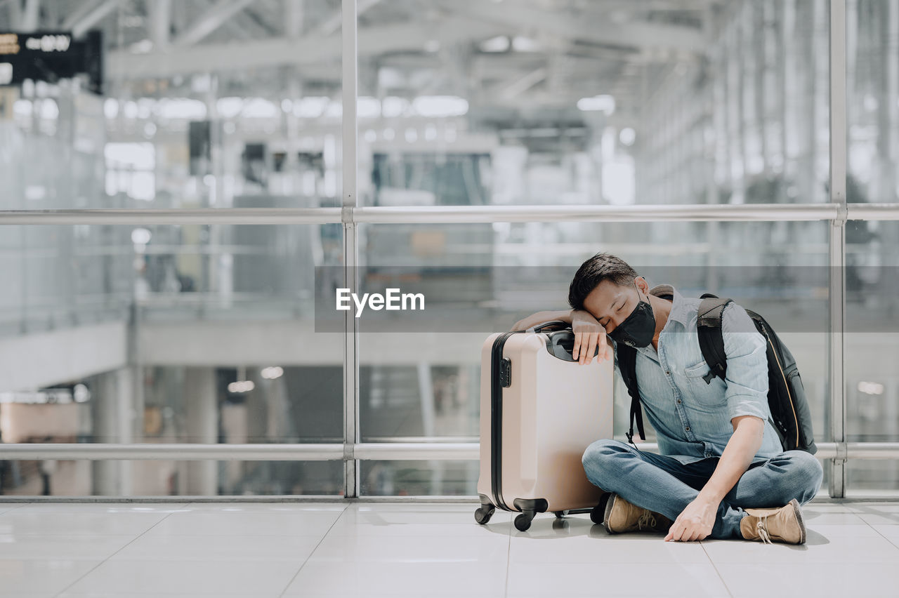 Full length of man sitting by suitcase at railroad station