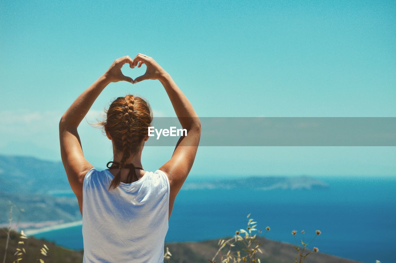 Rear view of woman making heart shape with hands against sea