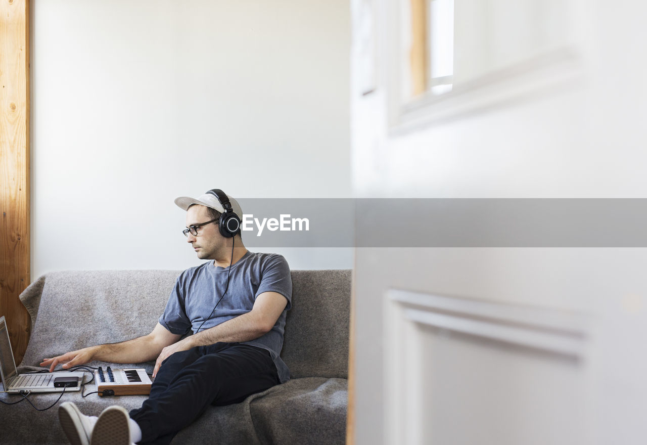 Man listening music while using laptop computer on sofa seen through doorway