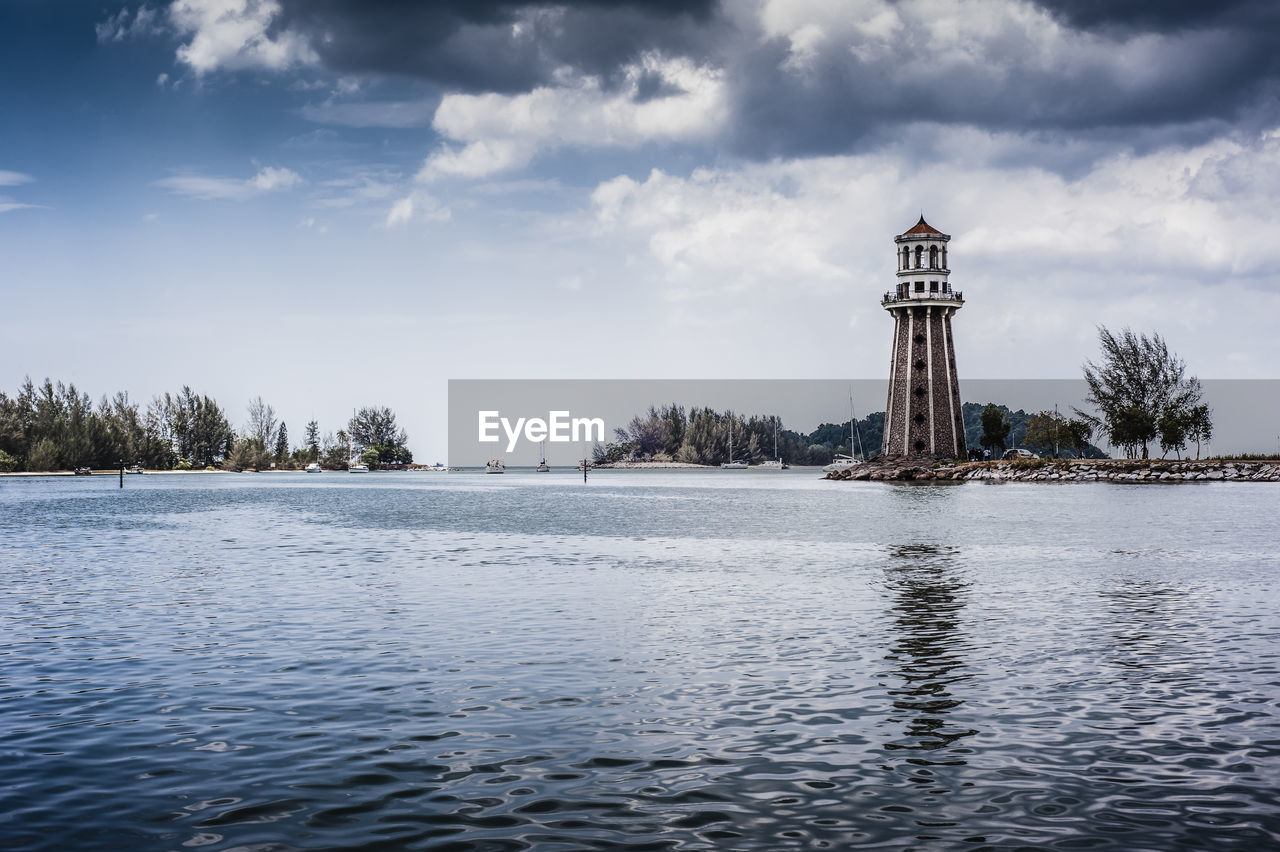 Lighthouse in sea against cloudy sky