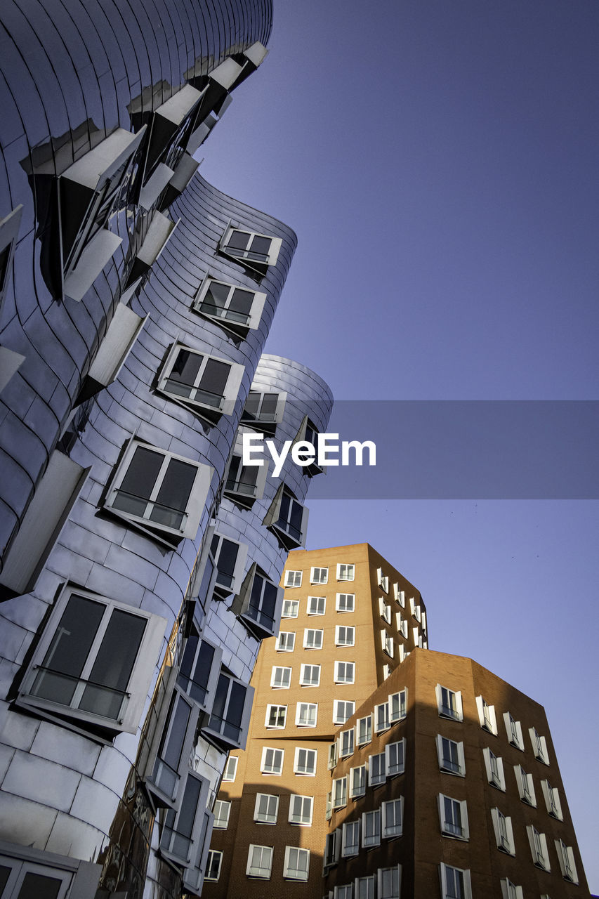 Low angle view of modern buildings against clear blue sky