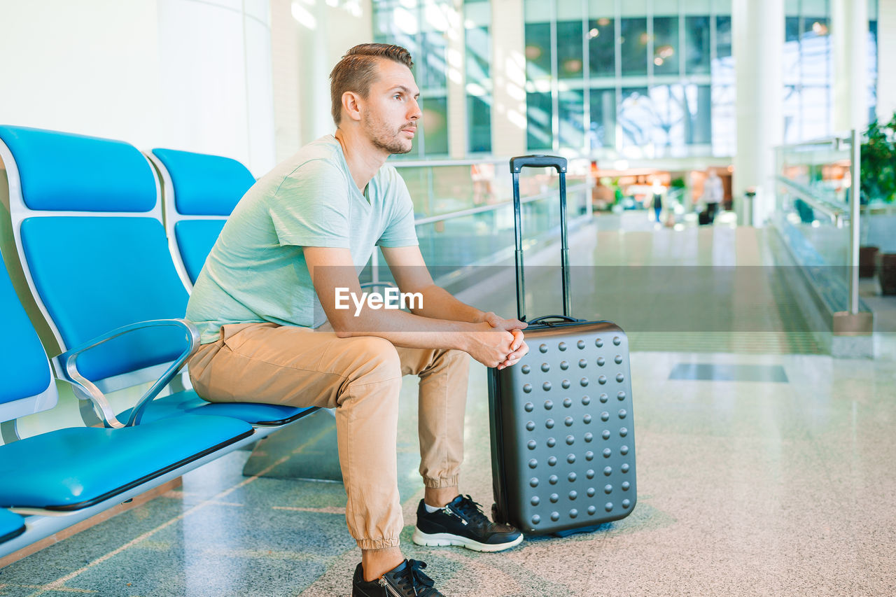 FULL LENGTH OF YOUNG MAN SITTING IN AIRPORT