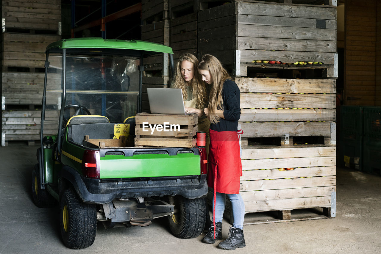Two women using laptop between crates on a farm