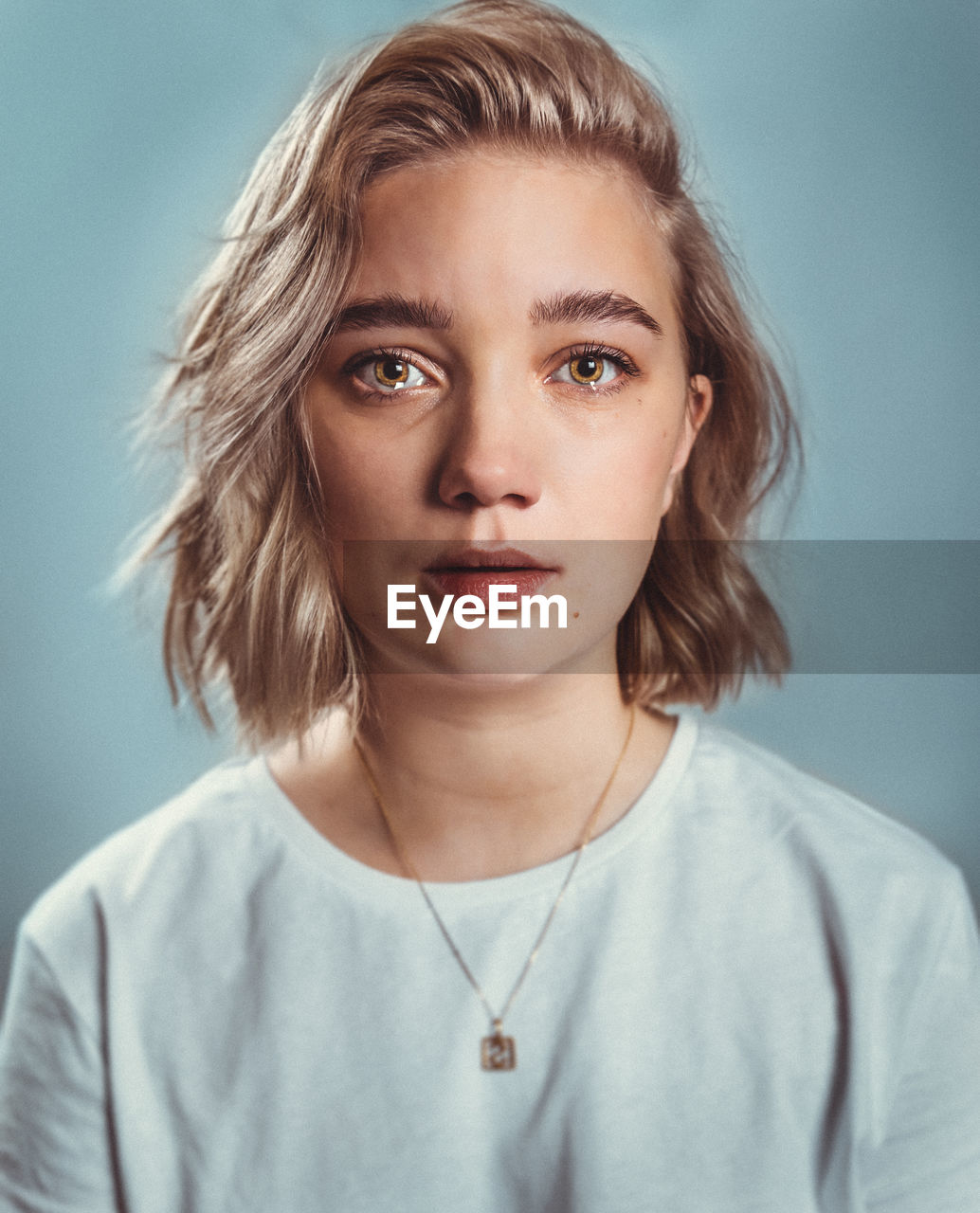 Portrait of young woman crying against gray background