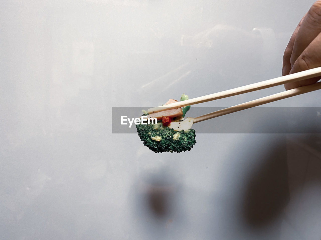 Close-up of person holding broccoli , chili pepper , garlic and bacon with chopsticks