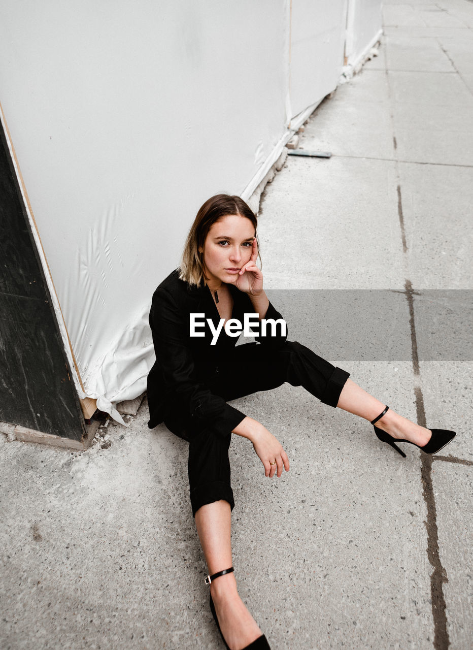 Portrait of young woman sitting against wall