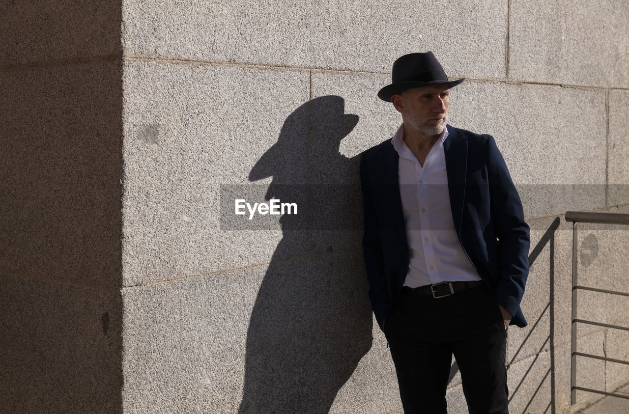 Portrait of adult man in hat and suit standing on street against wall. madrid, spain