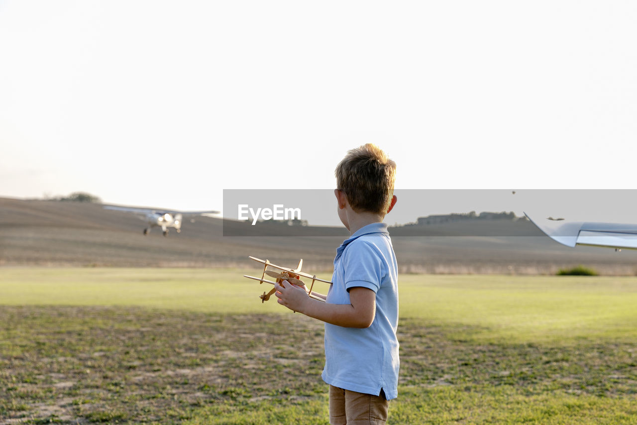 Little boy holding toy airplane while standing at airfield