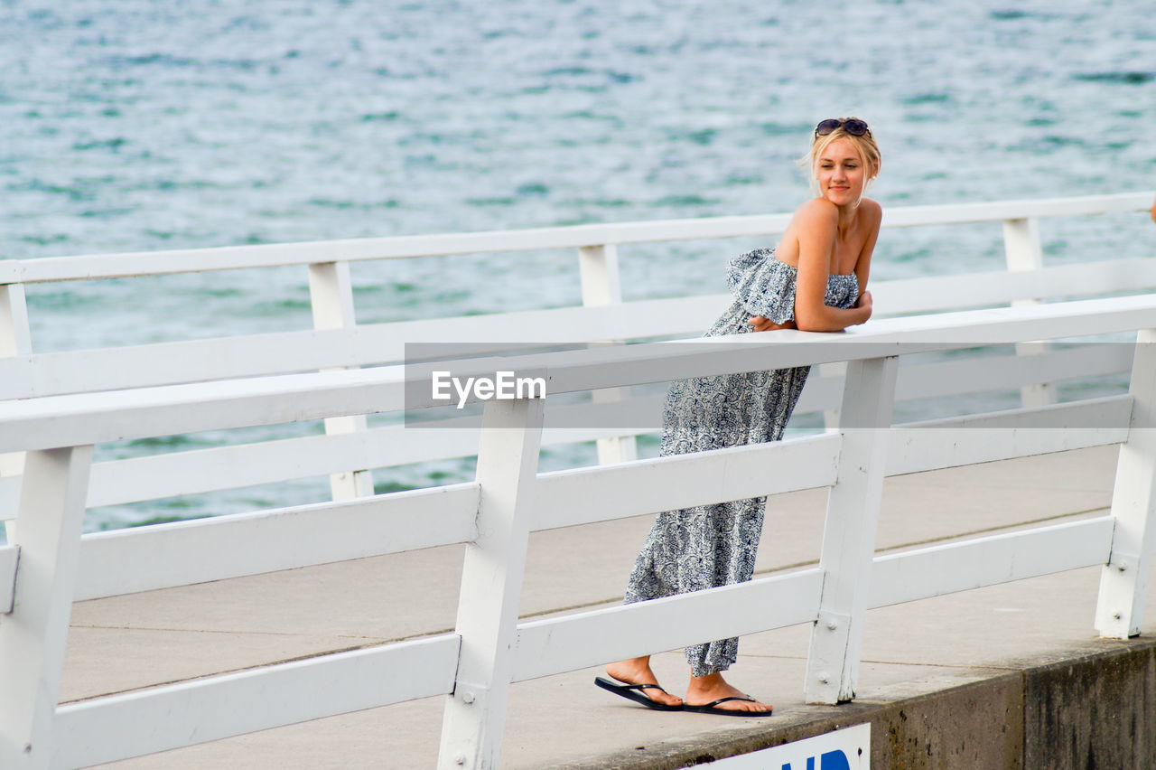 Full length on young woman leaning on railing at pier