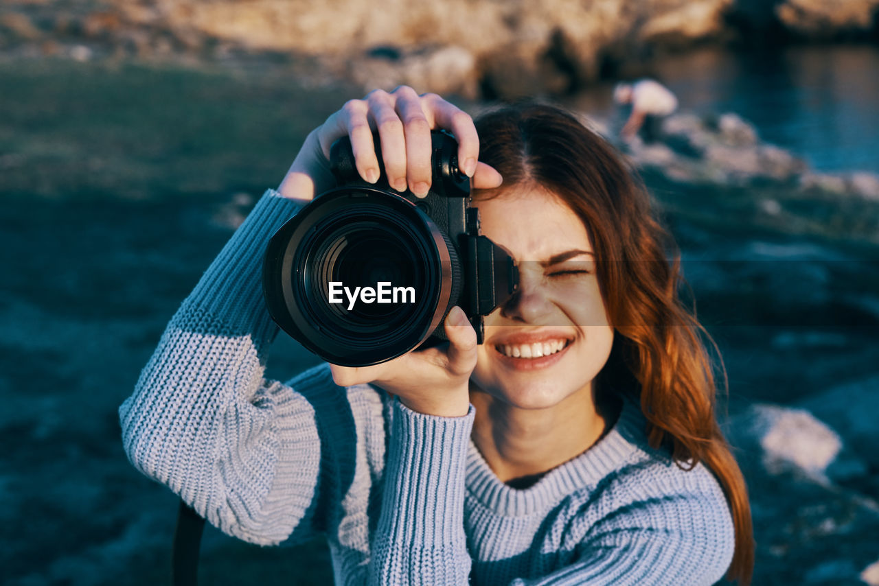 PORTRAIT OF SMILING WOMAN HOLDING CAMERA