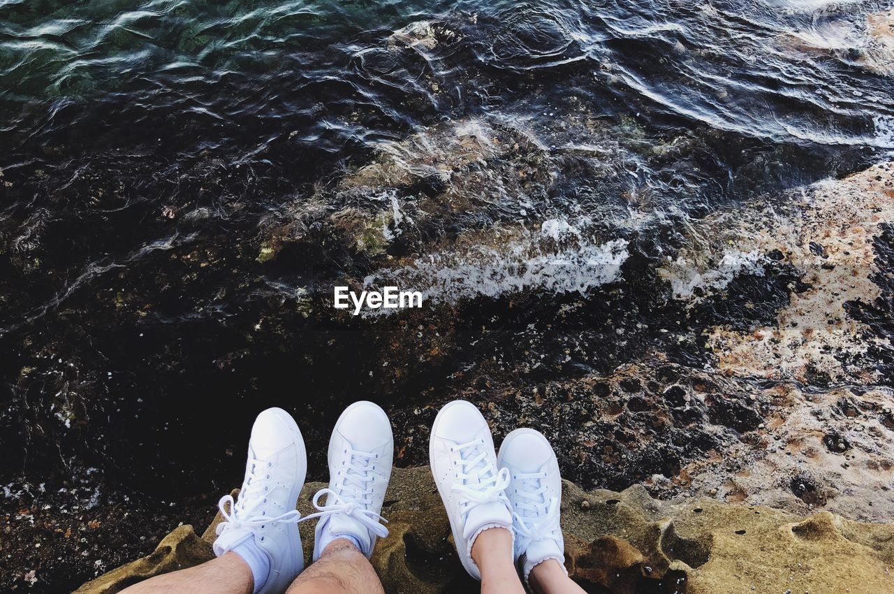 Low section of friends sitting on rock at beach